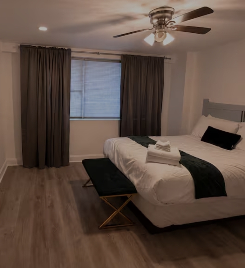 Furnished private bedroom with queen bed, bench seating, and soft lighting